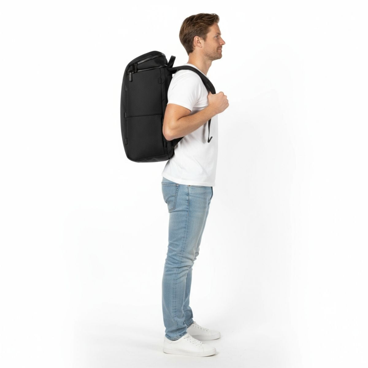 Man i vit t-shirt och jeans bär en svart Zeeksack-ryggsäck, sedd från sidan.