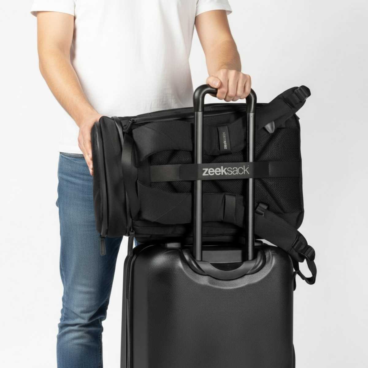 En svart ryggsäck sitter fast på handtaget till en kabinväska.