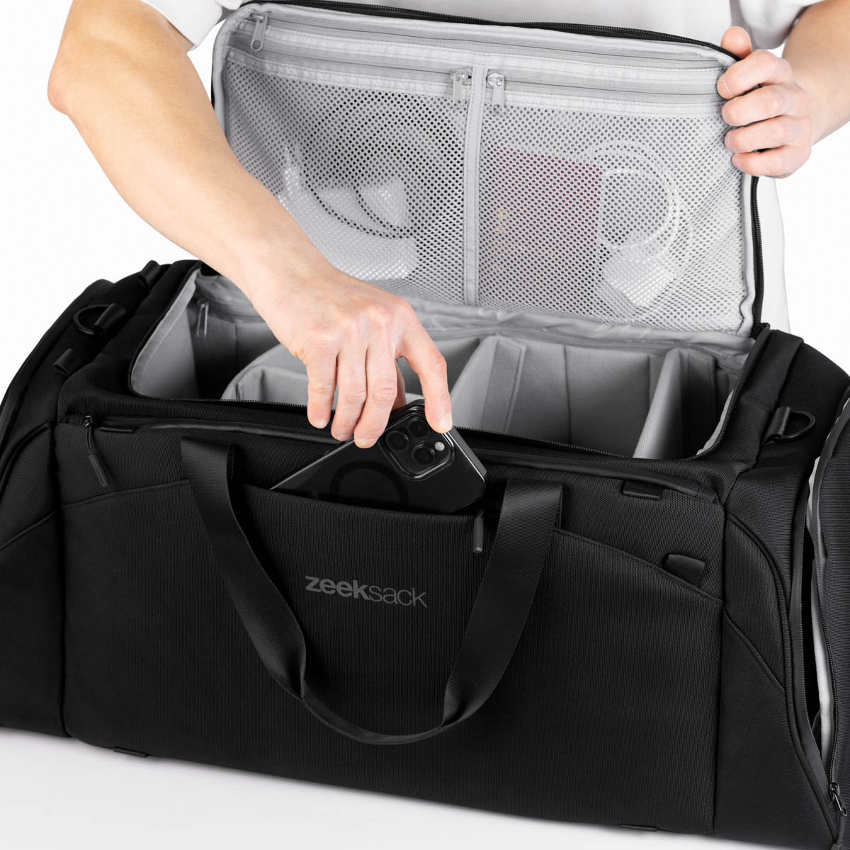 Man lägger ner telefon i ytterfack på svart duffelbag